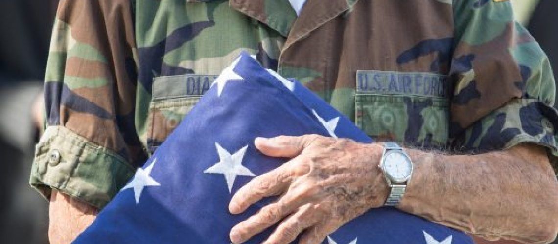 A man in a military uniform is holding an american flag.