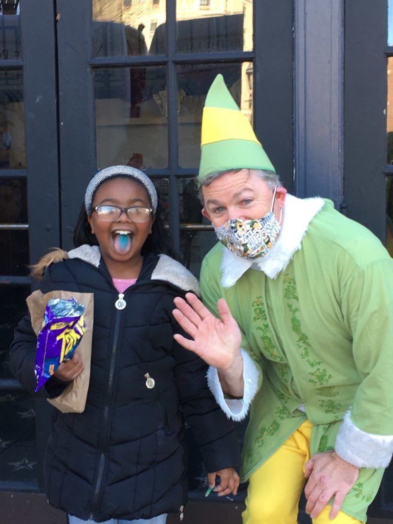 A man in a green elf costume is standing next to a little girl.