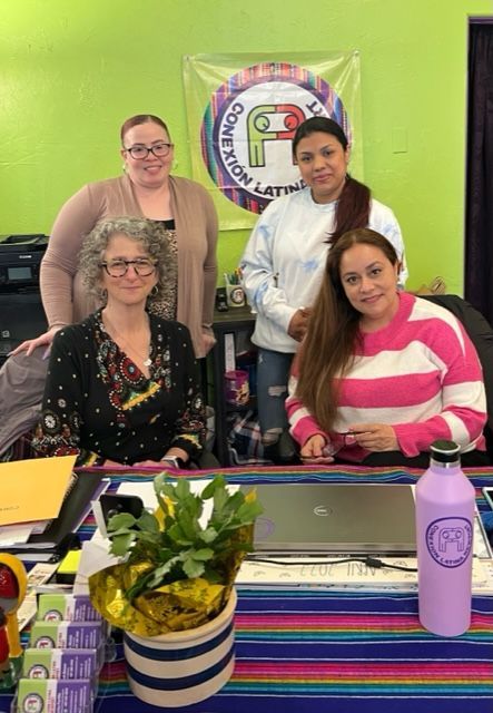 A group of women are posing for a picture while sitting at a desk.