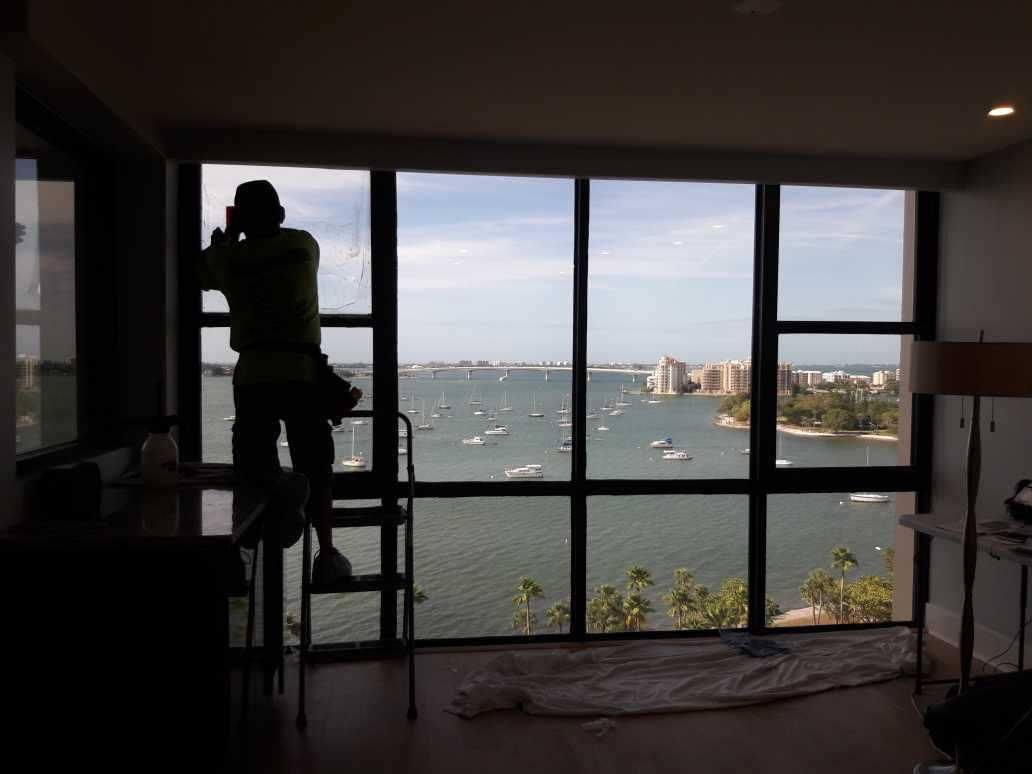 Person on a ladder painting a wall inside a room with a waterfront view through large windows