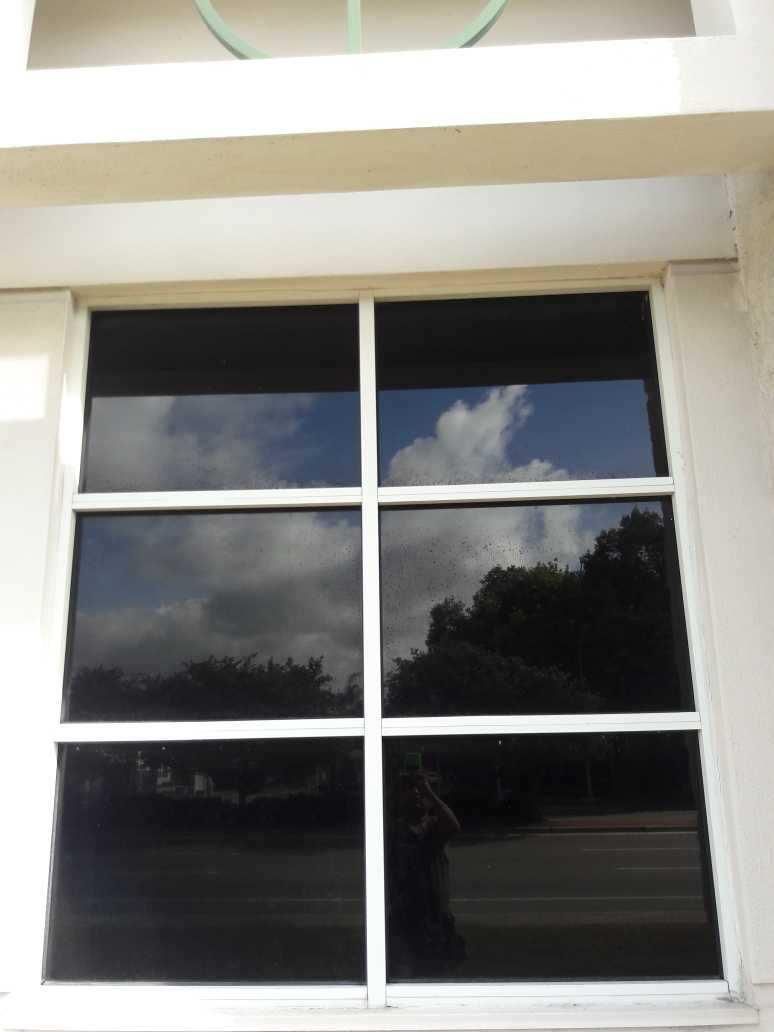 White-framed window reflecting clouds and trees against a light exterior wall