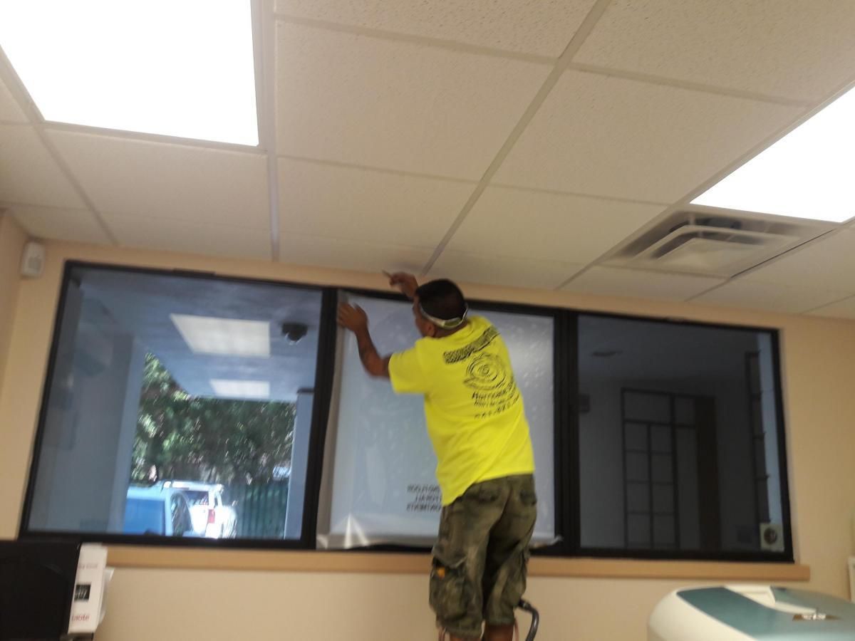 Worker in yellow shirt installing a window frame in an office interior.