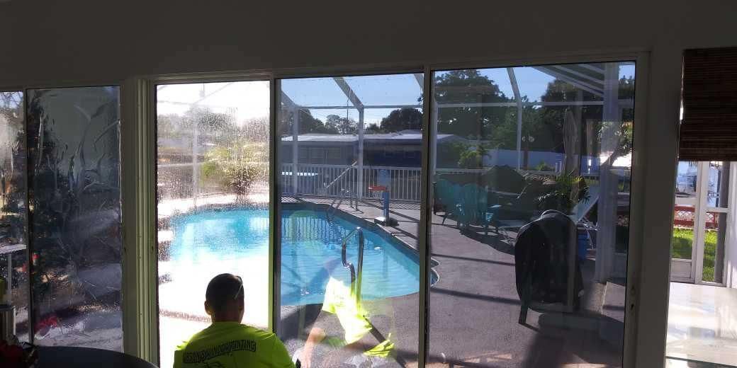 Person sitting by a screened patio looking out at a backyard pool and lawn.