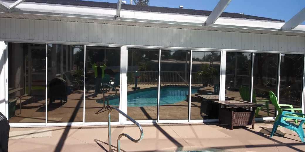 Patio with screened enclosure around a swimming pool, lounge chairs, and a small table beside the house