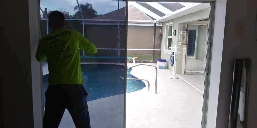Person in a neon green shirt standing by a sliding glass door, looking out to a patio and pool.