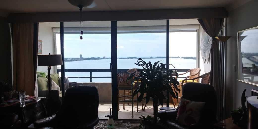 Living room facing a balcony and ocean view, with chairs, a plant, and curtains.