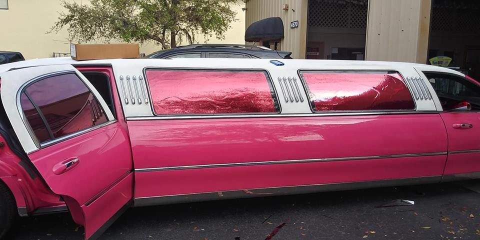 Pink stretch limousine parked with its rear door open outside a building