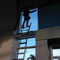 Person on a ladder reaching toward a high window inside a modern building.