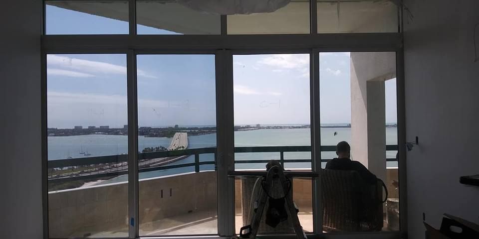 Interior view of a waterfront room with large windows, chairs, and a balcony overlooking water and sky