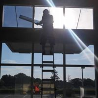 Silhouetted worker on a ladder cleaning tall glass windows in bright sunlight
