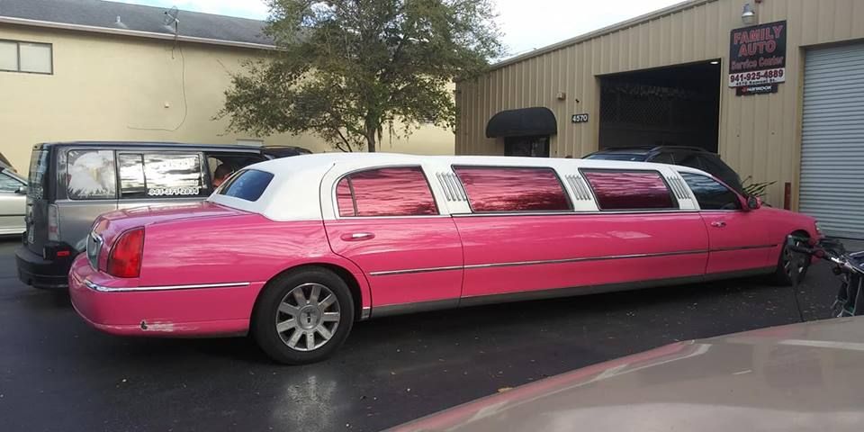 Pink stretch limousine parked outside a building, with a dark SUV beside it.