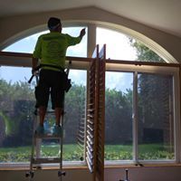Worker on a ladder cleaning the top of a large arched window inside a room