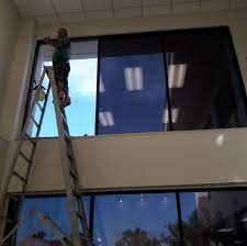 Person on a ladder cleaning a large window inside a room