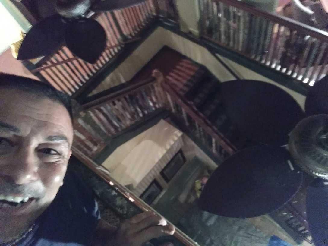 Man smiling in a room with mirrored ceiling and bookshelves, with two ceiling fans overhead