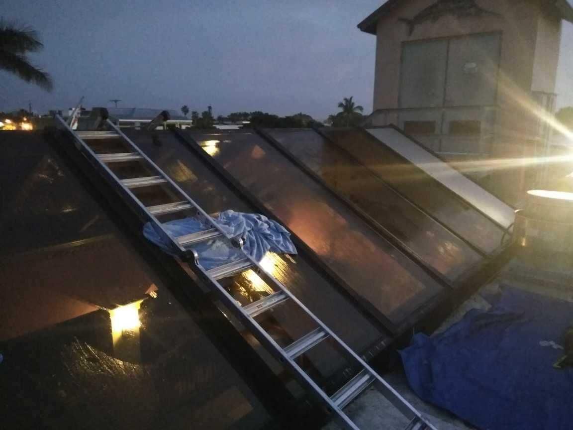 Solar panels on a tilted rooftop at dusk, with a ladder leaning across the panels.