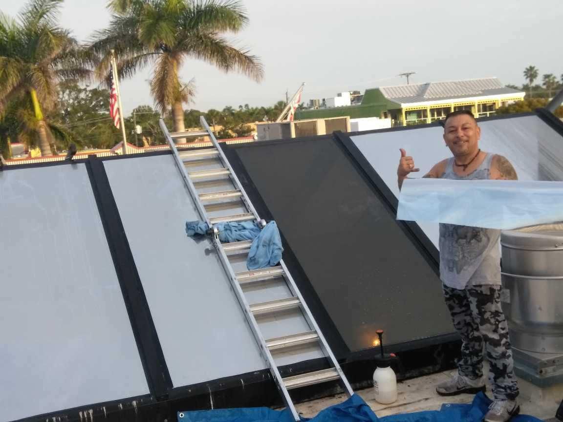 Man on a rooftop beside solar panels, smiling and giving a thumbs-up at sunset