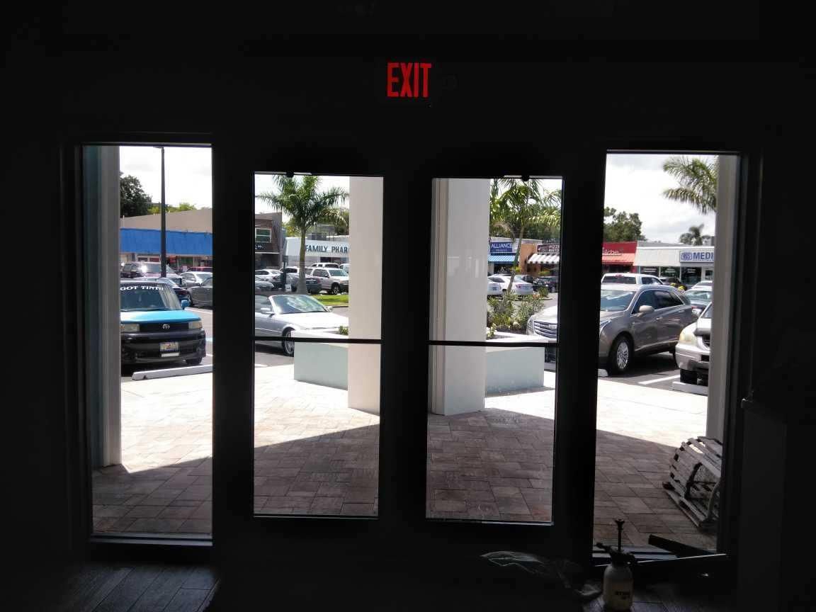 Glass storefront doors with an EXIT sign, showing a parking lot outside.