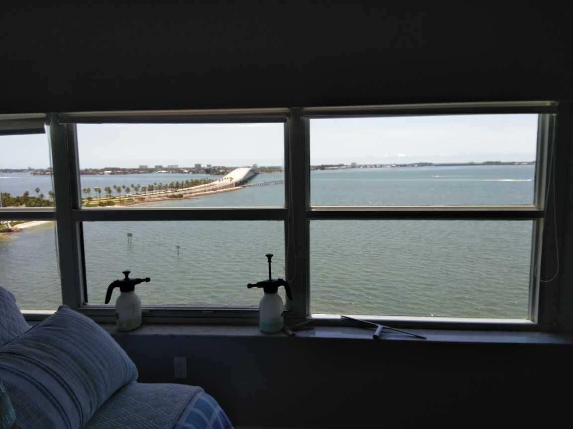 View through a window of calm water and a distant shoreline, with a blue sofa and two small lamps inside