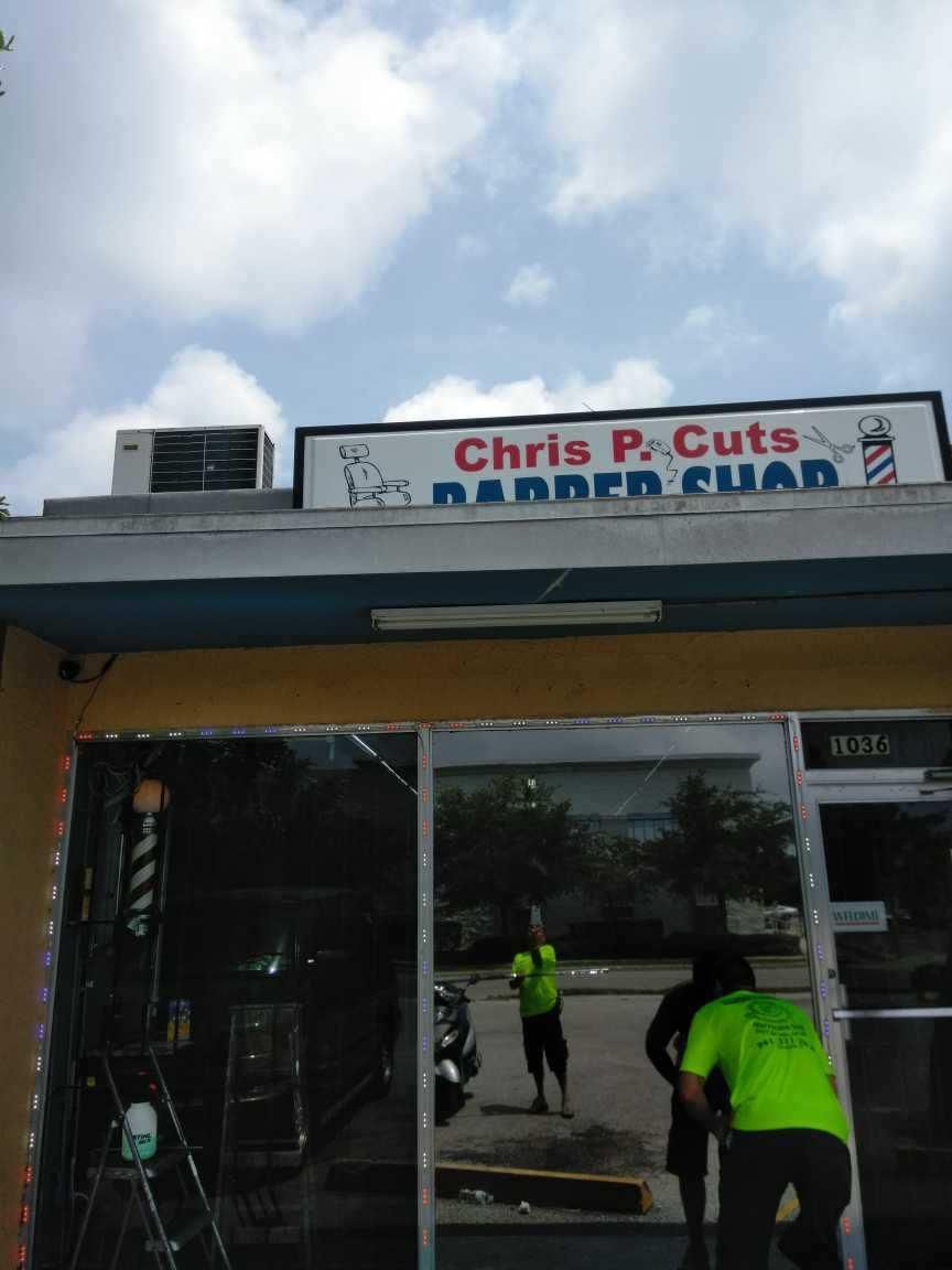 Exterior of Chris P. Cuts barber shop with two workers in neon safety shirts cleaning the entrance