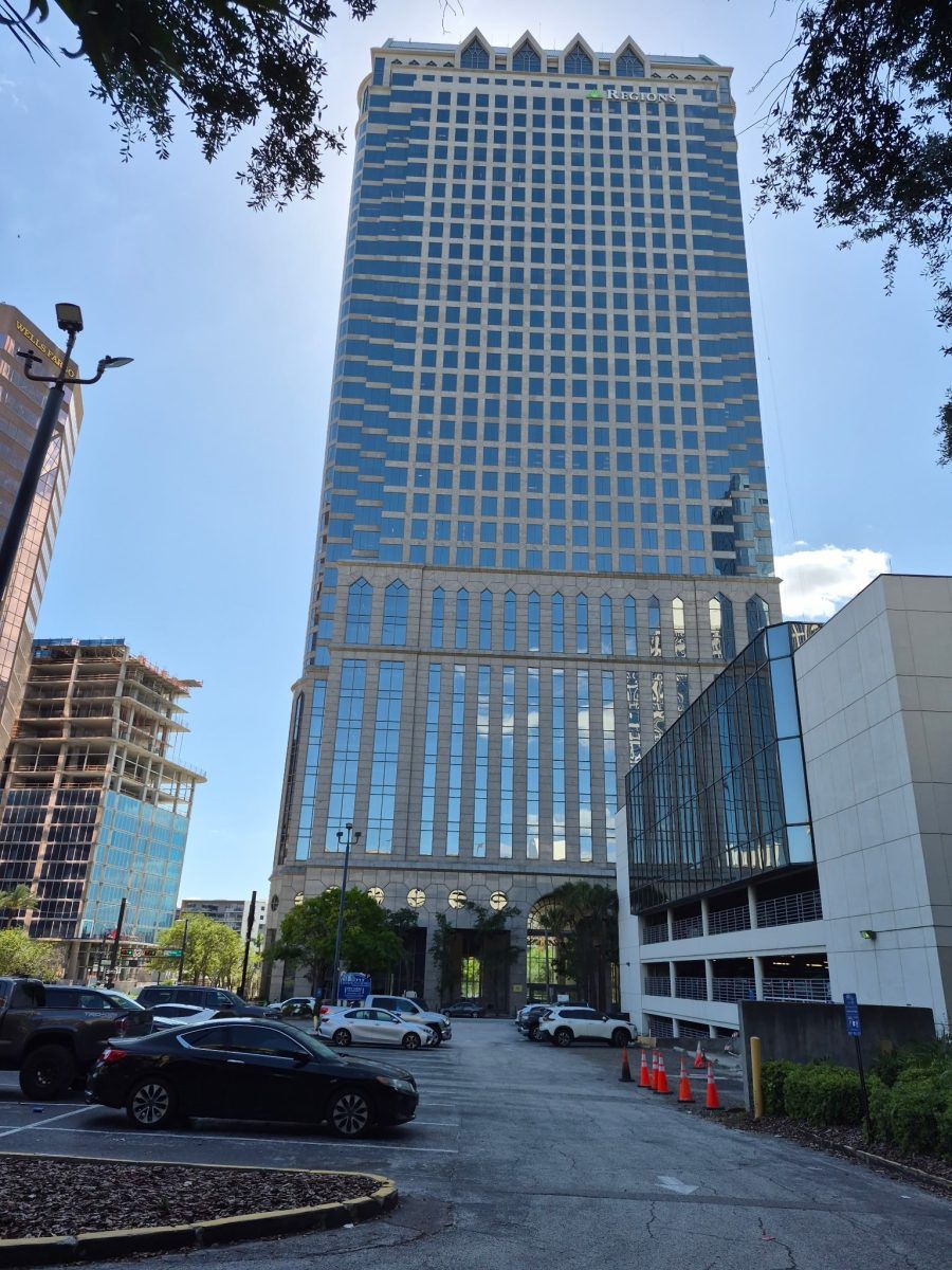 Tall modern glass office tower with a decorative roof, viewed from a parking lot on a sunny day