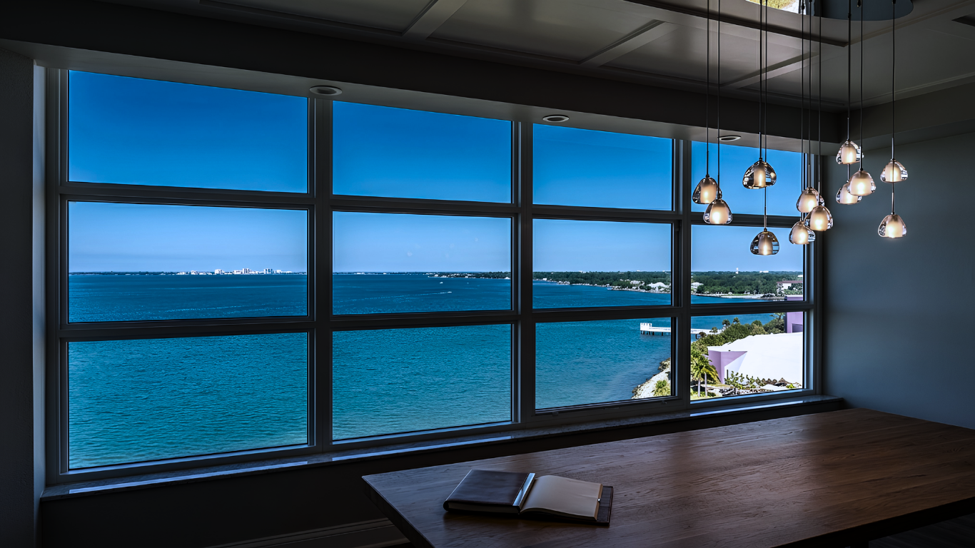Three tall windows framing a sunny outdoor view of blue sky, clouds, and buildings.