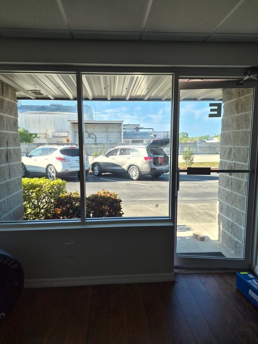 Interior room looking out through large windows and a glass door at parked cars outside.