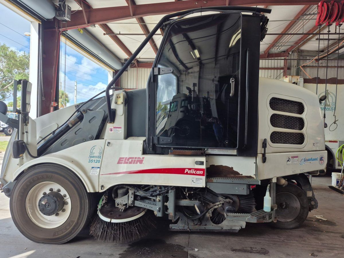 White compact street sweeper parked under a metal-roofed shed