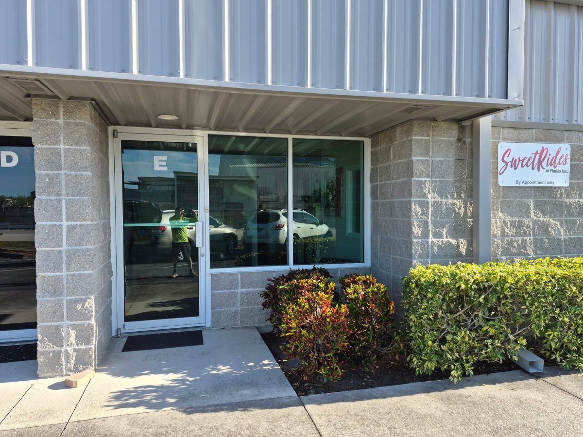 Storefront entrance with glass door, window, and hedge under a metal awning