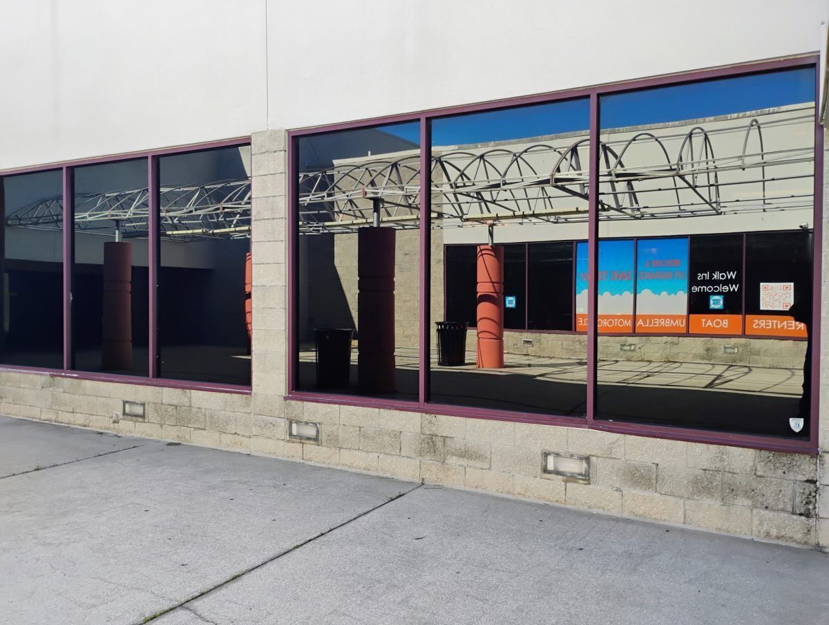 Storefront windows covered with barbed wire reflections and blue-orange signs, viewed from a sidewalk