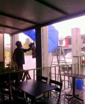 Person adjusting laundry under a covered patio with tables, chairs, and a blue tarp nearby