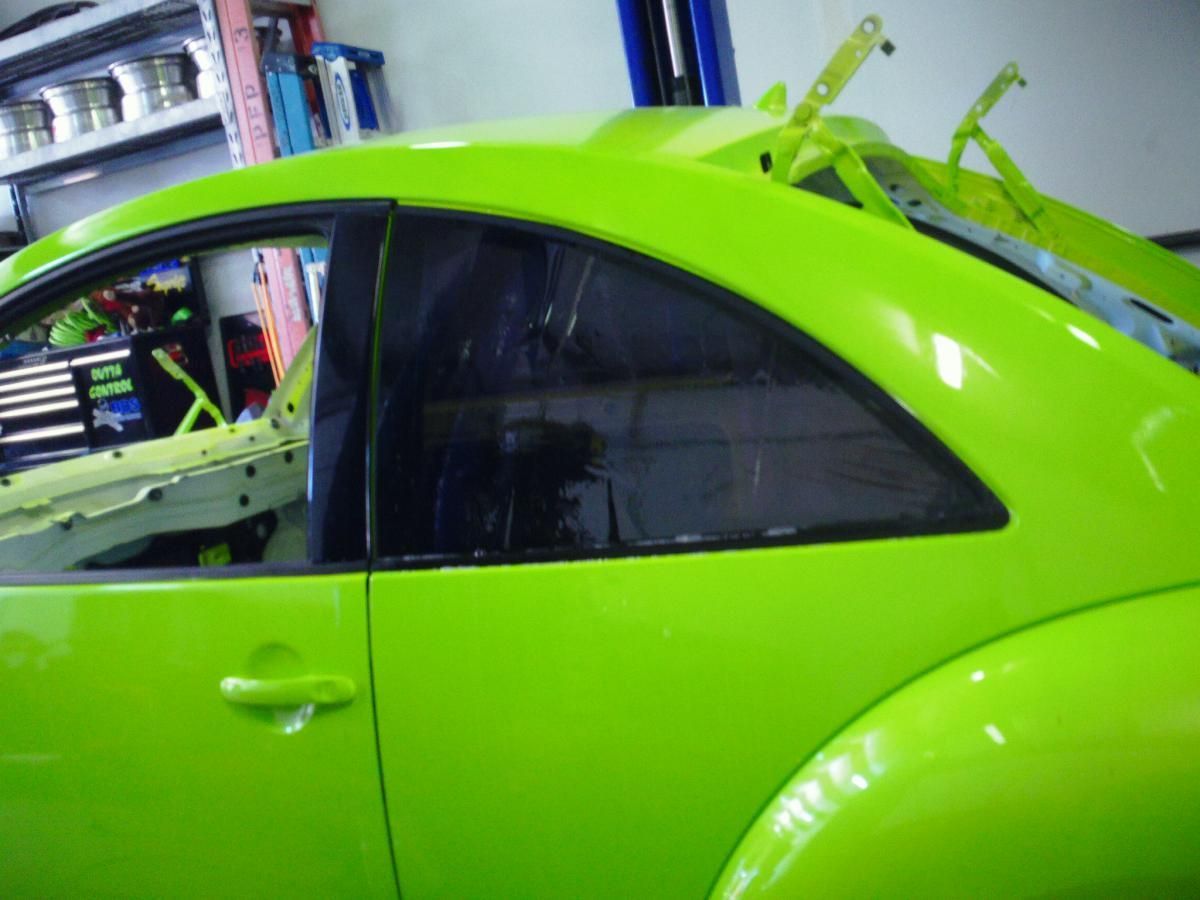 Bright green car in a garage, shown from the side with a raised rear hatch.