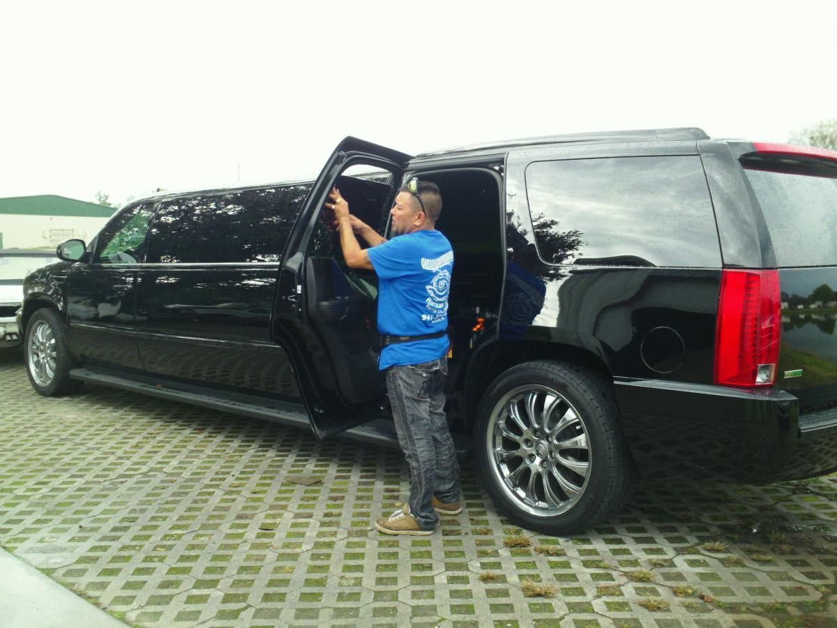 Black stretch SUV with open rear door on a paved lot; a man in a blue shirt stands by the door.