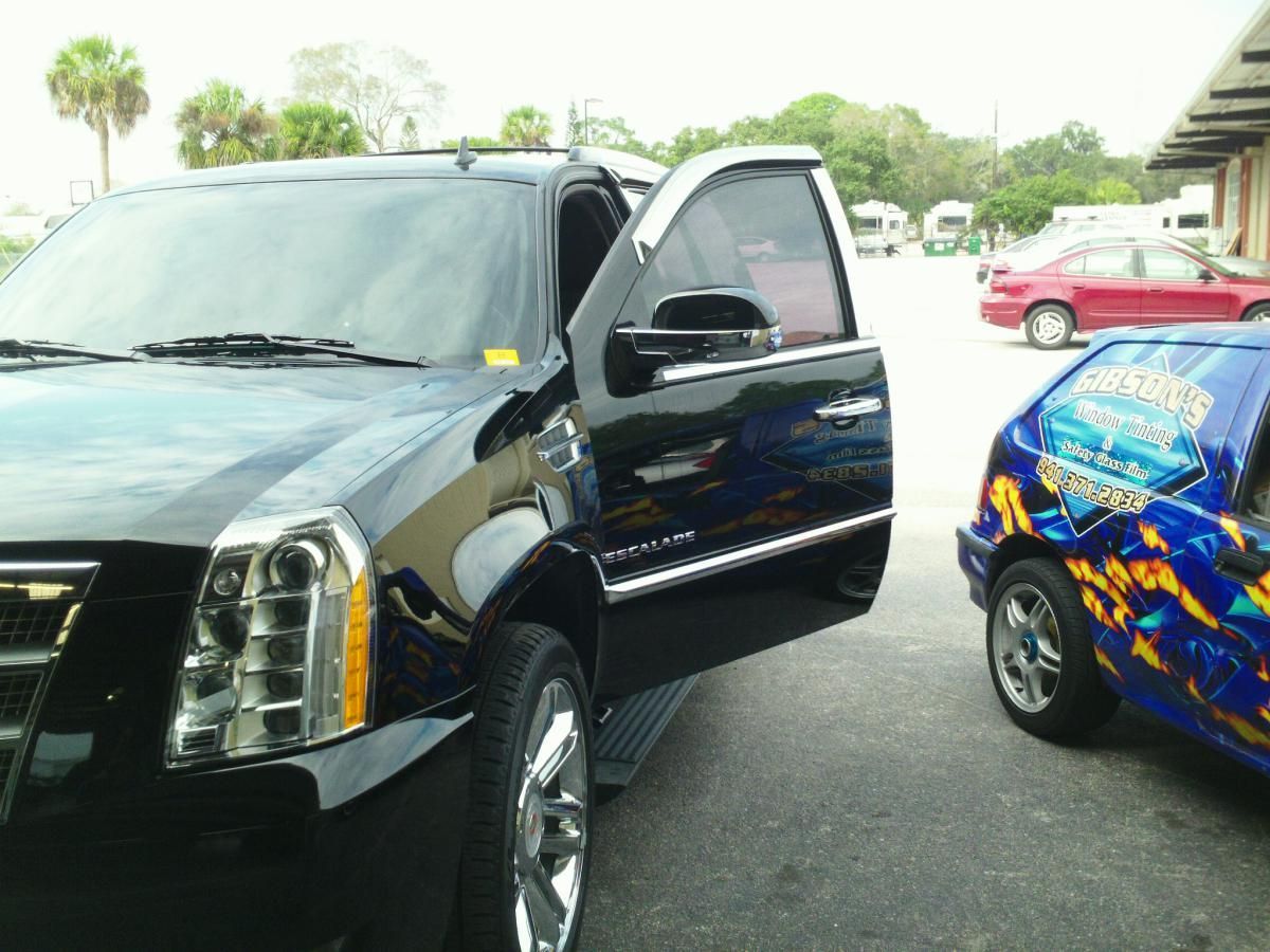Black SUV with open door parked beside a blue custom car in a lot