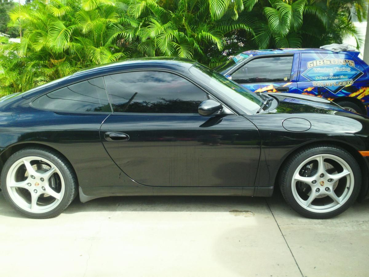 Black two-door sports coupe parked on a driveway, side view, with a blue car behind it.