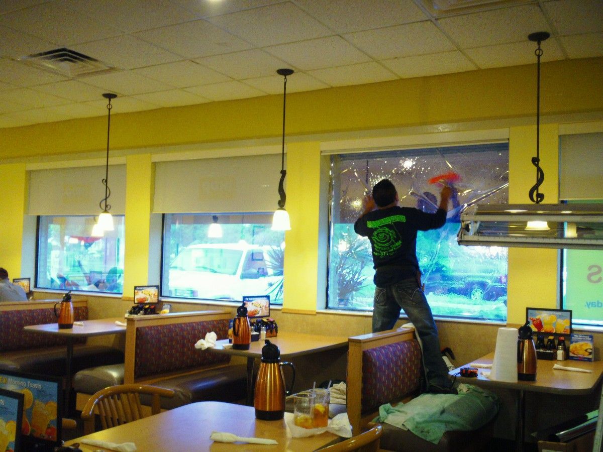 Person cleaning windows in a bright restaurant dining room with booths and tables.