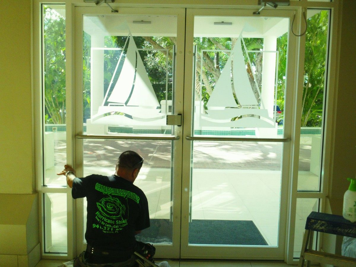 Person seated by glass entrance looking out at sailboats on the water