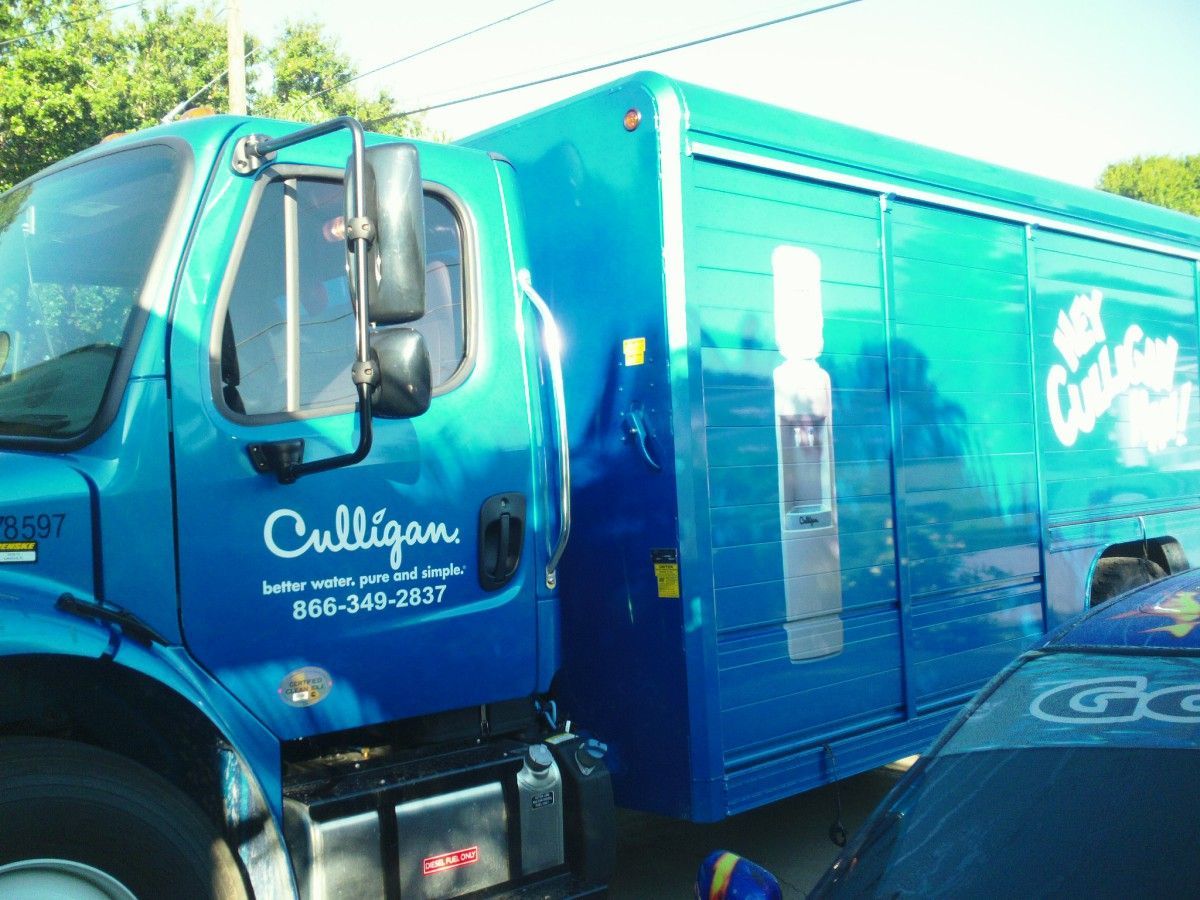 Blue Culligan water delivery truck parked on a street in bright sunlight