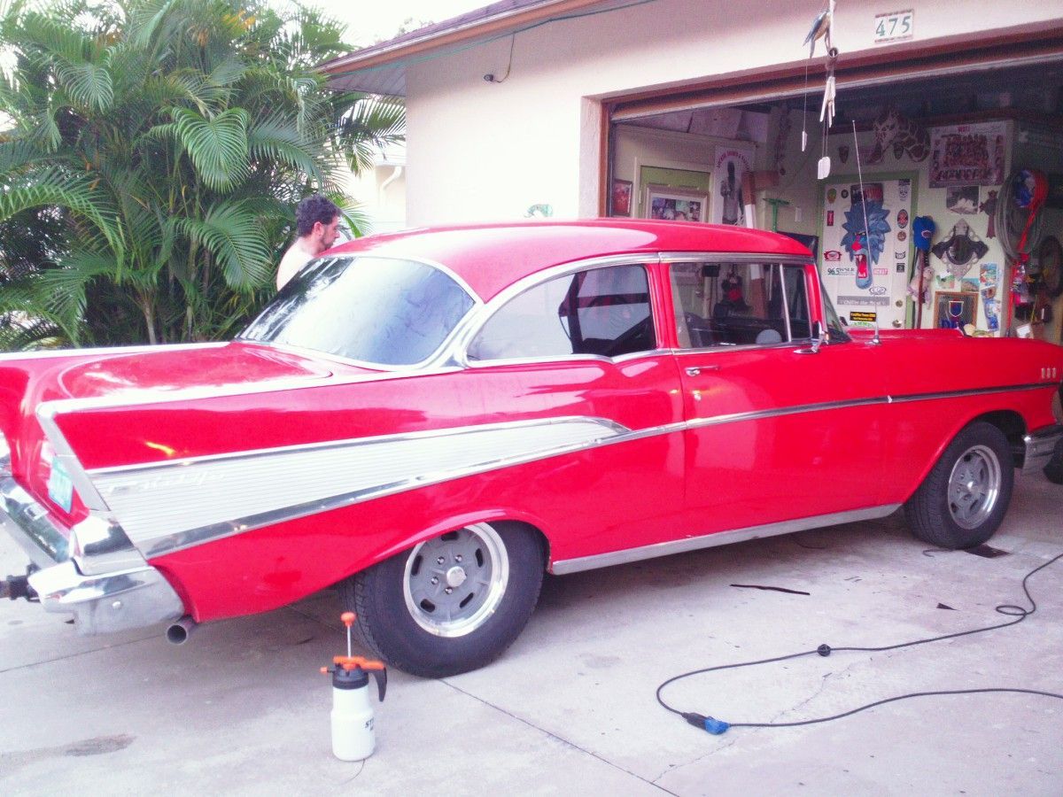 Red classic car parked in a driveway beside a house, with white diagonal side stripes.