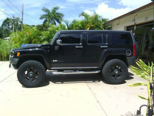 Black Hummer SUV parked in a driveway beside a house with palm trees