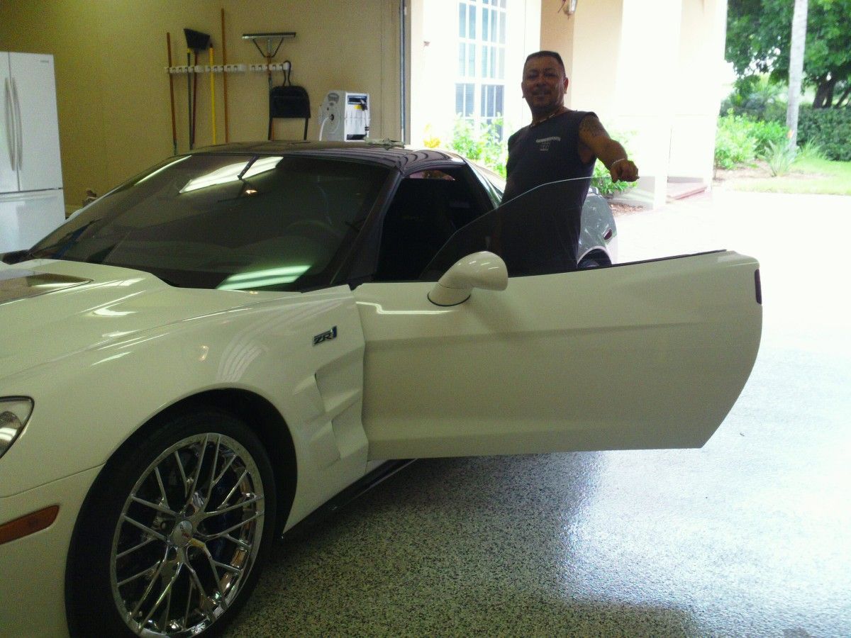 White sports car in a garage with the driver’s door open and a man standing beside it