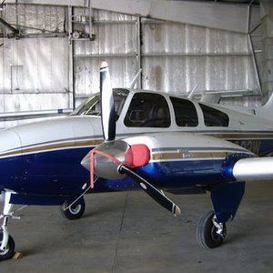 Small blue-and-white twin-engine airplane parked inside a hangar with a red propeller cover