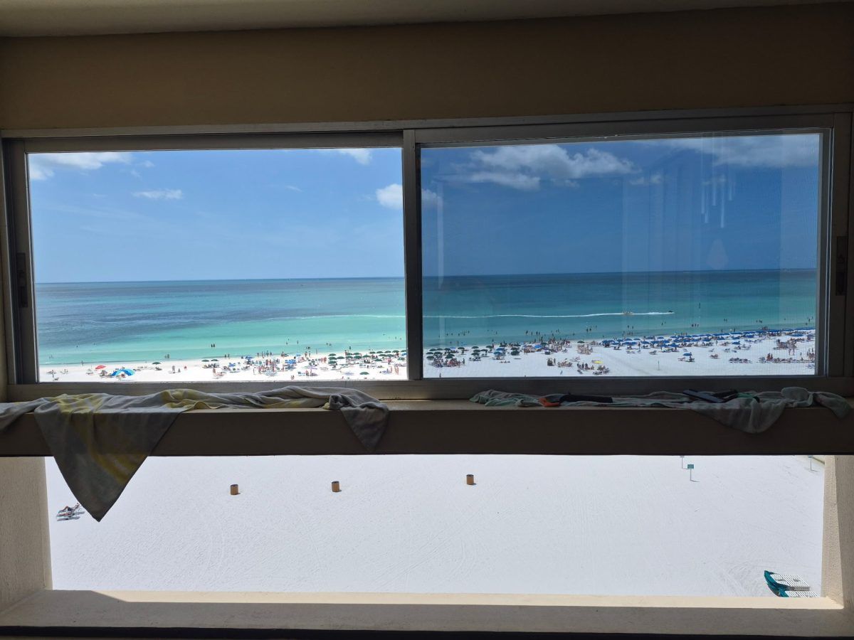 Ocean view through a window above a beach with blue water and a few umbrellas.