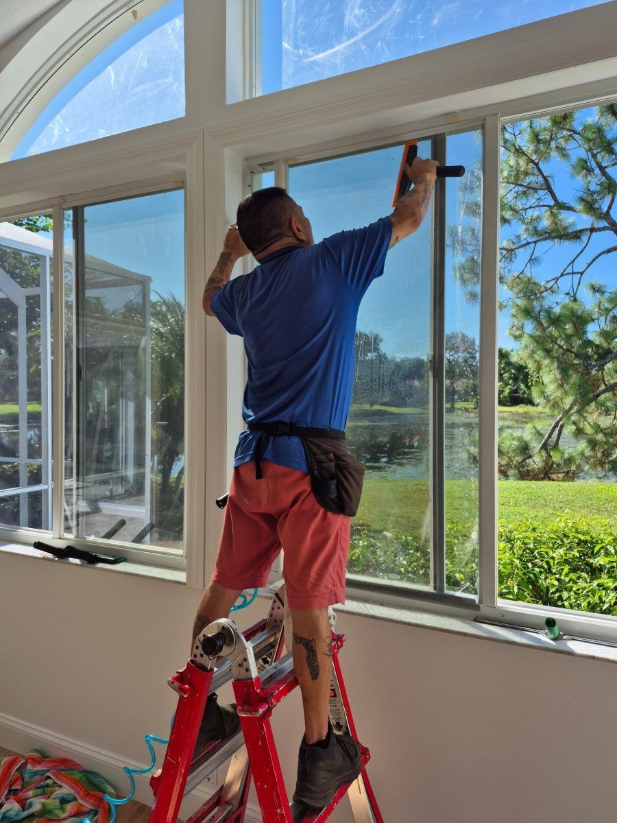Person on a ladder installing or cleaning a large window in a bright room.