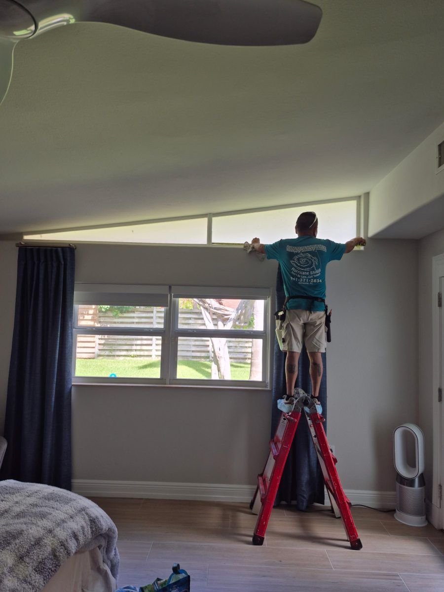 Person on a red ladder measuring a high window in a gray bedroom