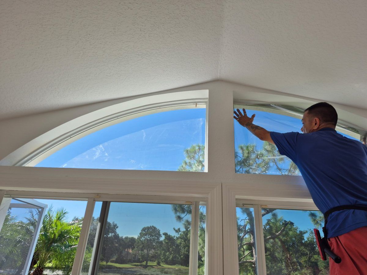 Man installing a blue window shade on a large arched window in a bright room
