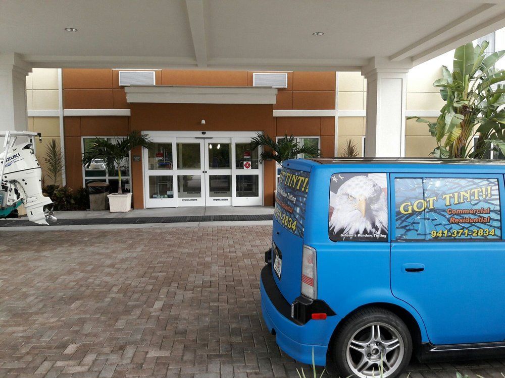 Blue van parked under a hotel entrance canopy with glass doors and brick driveway