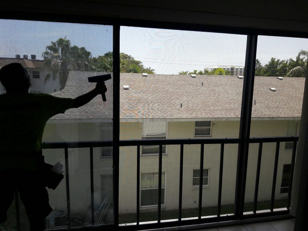 Silhouette of a person spraying cleaner on a sliding glass door, with an apartment building visible outside.