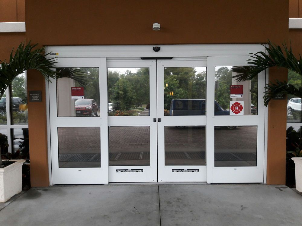 White glass double doors at a building entrance with potted plants on both sides.