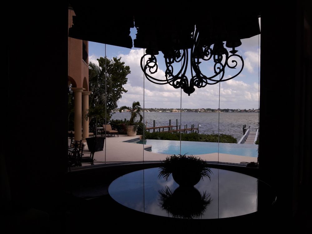 Covered patio overlooking an infinity pool and ocean, with a round table and ornate chandelier in the foreground