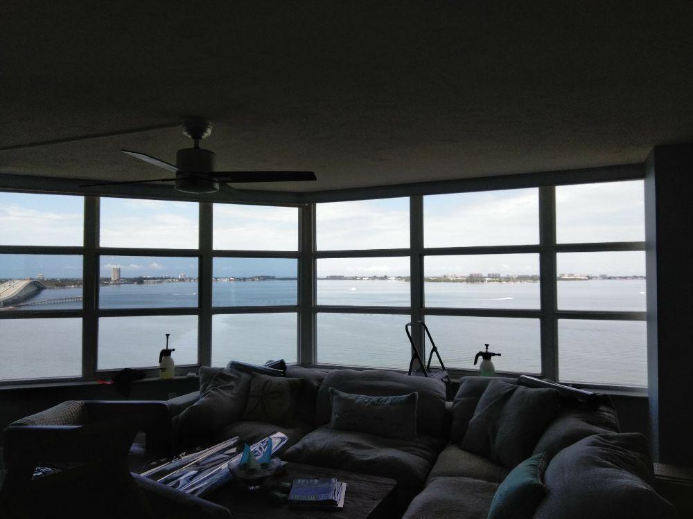Curved living room windows overlooking a calm bay at sunset, with a sectional sofa in the foreground